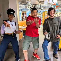 3 teens in a spiderman pose in the YA section of library